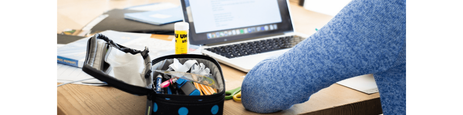 Banière matériel pédagogique Photographie d'une personne de dos qui utilise un ordinateur portable avec une trousse et du matériel de bureau situé à coté de l'ordinateur